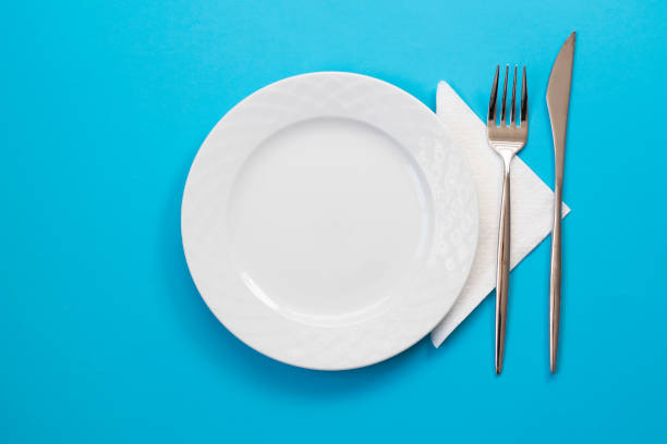 istock Empty white plate with fork, knife and napkin on blue background. Top view. 1303192522