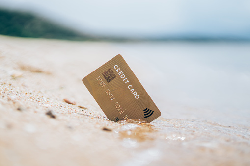 Gold contactless credit card stuck in the sand on seaside.