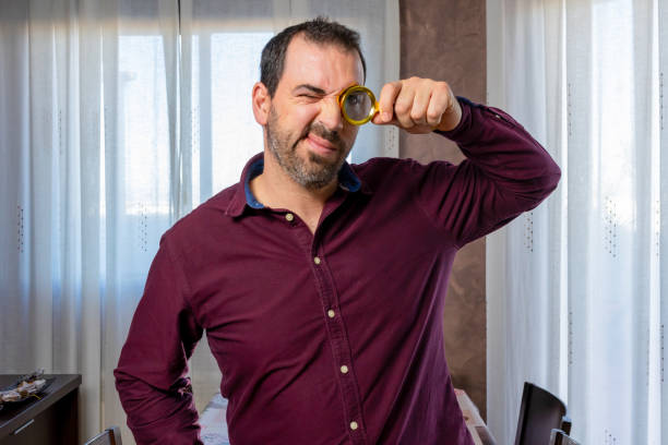 bearded man in a purple shirt looking through a golden magnifying glass - spy secrecy top secret mystery imagens e fotografias de stock