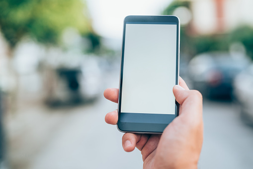 Man holding mobile phone with isolated screen on the background of a city street.