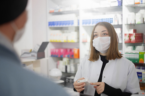Young pharmacist wearing a mask while talking with a customer