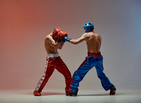 Sparring of athletic guys fighting, boxers training in red studio light, mixed fight workout. High quality photo