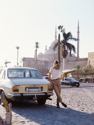 Woman in headscarf standing near the vintage car on the background of Mosque of Muhammad Ali