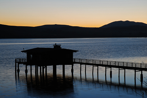 A pier and fishing house is silhouetted against the blued bay waters