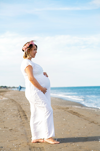 Beautiful Pregnant Woman with White Dress on the Beach