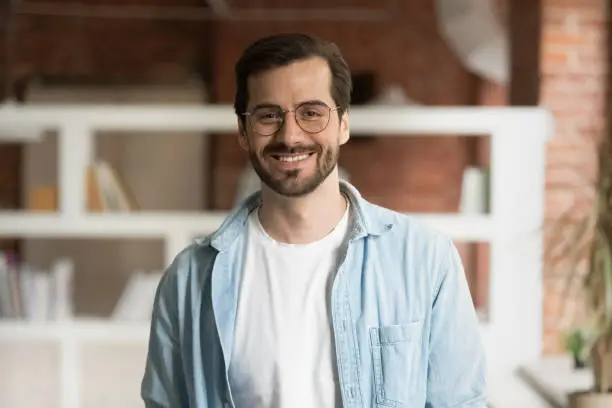 Portrait of smiling millennial Caucasian male tutor or coach wear glasses pose in modern office of classroom. Headshot of happy young man employee satisfied with work job. Employment concept.