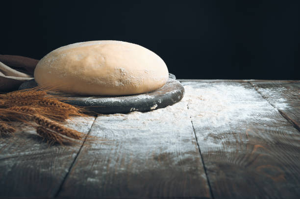 istock Round dough on a board in flour and wheat on a dark background 1303209761