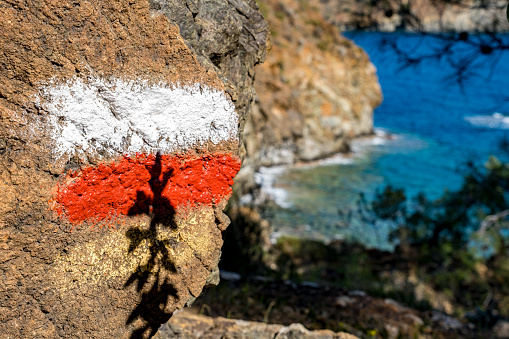 A walkway painted on the rock, a directional sign, with the shadow of the plant on it. Background mediterranean landscape