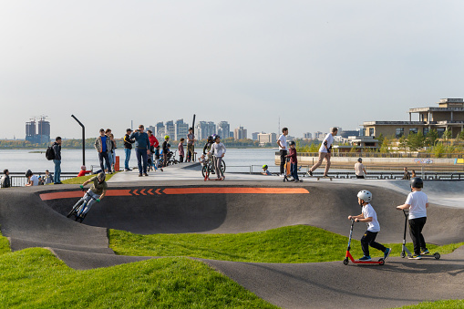 Kazan, Russia-September 26, 2020: Walking residents in the city park on the embankment, groups of children and teenagers in protective helmets on scooters and bicycles on the ride area.