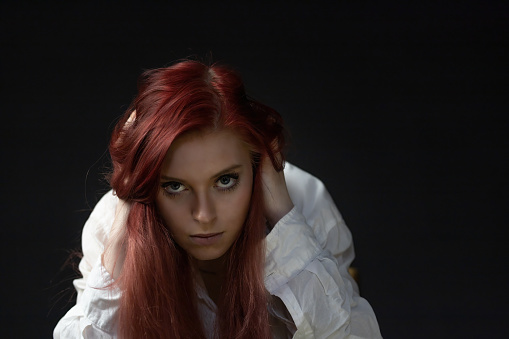 Low key portrait of beautiful redhead young woman in trouble looking at the camera.  Horizontally.