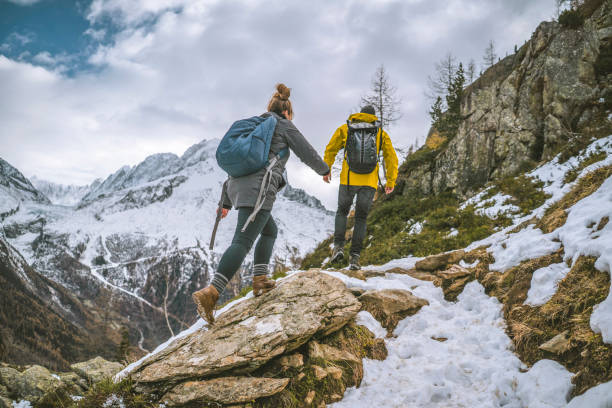 Young couple of hikers bound up ridge together Snowcapped mountains behind backpacking stock pictures, royalty-free photos & images