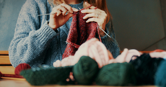 Female hands holding knitting needle. Woman knitting homemade toys in dark room under lamp. Diy hobbies.