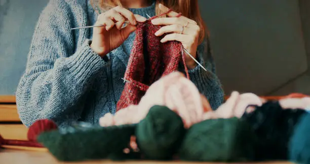 An unrecognizable woman is in the process of knitting a new scarf. She's enjoying moments of silence while focusing and skilling up.