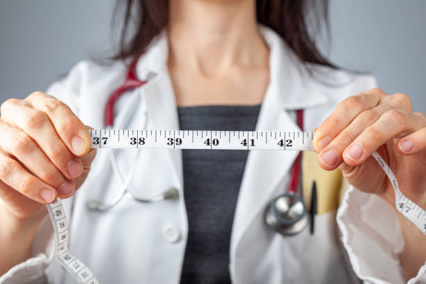 doctor with tape measure highlighting abdominal circumference Close up isolated image of a caucasian doctor holding a tape measure in her hands which shows 40 inches as abdominal circumference upper limit in healthy people. Concept for weigh loss and fitness. dieting stock pictures, royalty-free photos & images