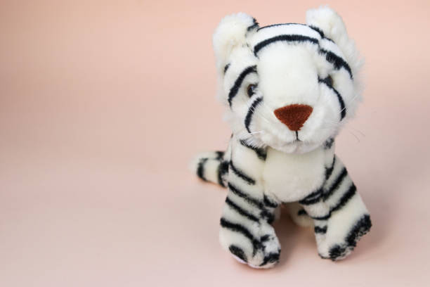 istock Toy white tiger cub on peach background with reflection of shadow 1303223940