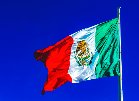 On a bright sunny day the Mexican flag waves against a blue sky over Avenida Quinta in Playa del Carmen, Mexico.