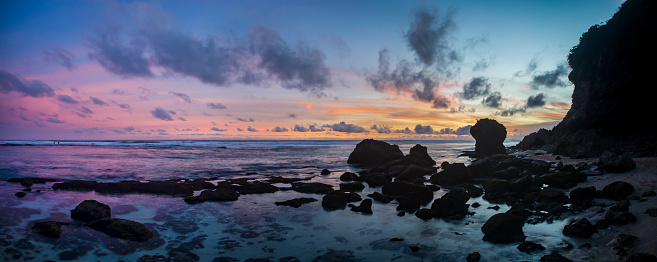 Panoramic sunset along a rocky white sand beach in the southern coast in Bali in Indonesia in long exposure mode.