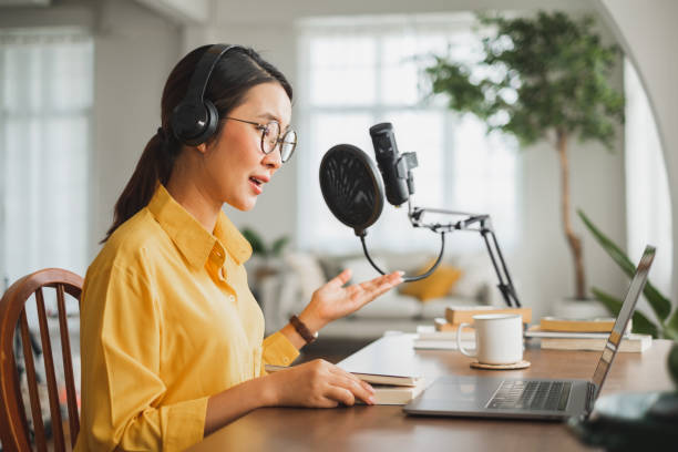 istock Asian woman recording a podcast on laptop computer with microphone while online live streaming at home 1303246066