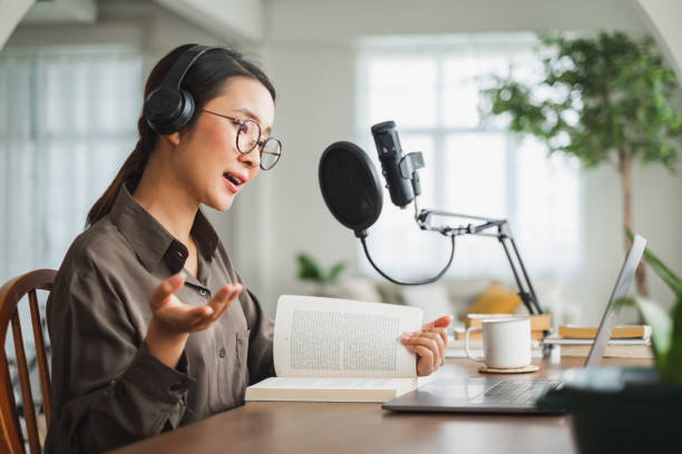 Asian woman recording a podcast on laptop computer with microphone while online live streaming at home