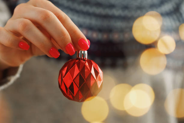 main d’une femme dans le chandail festif retenant la babiole de noël avec les lumières brouillées - christmas ball christmas ornament human hand photos et images de collection