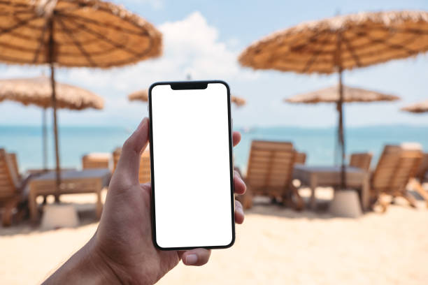 istock a man holding mobile phone with blank desktop screen while sitting on the beach 1303255447