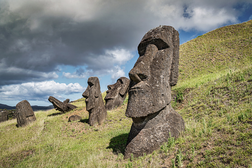 Easter Island - Rapa Nui Moai Statues at Rano Raraku hills under dramatic sunny summer cloudscape. Rano Raraku is a volcanic crater formed of consolidated volcanic ash. Terevaka, Rano Raraku, Rapa Nui National Park, Hanga Roa, Easter Island, Chile, Oceania