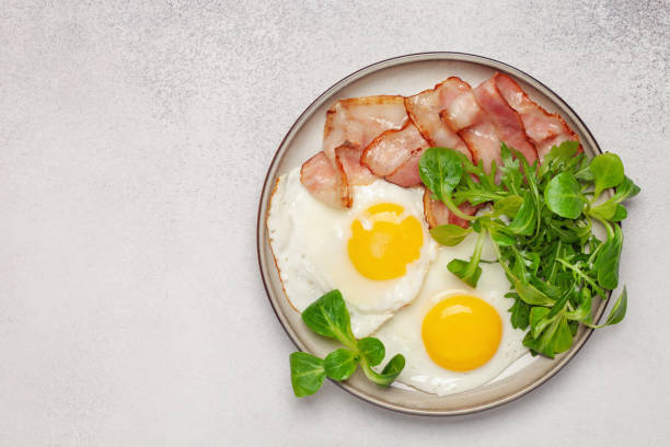 istock Continental breakfast - fried eggs, bacon and lettuce leaves in a plate on a bright background. Top View 1303258251
