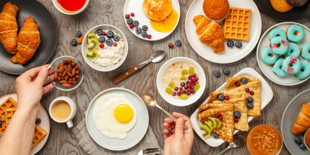 istock Continental breakfast captured from above (top view, flat lay). Coffee, tea, croissants, jam, egg, pancakes, maffins and oatmeal. Wooden background. Family breakfast table. 1303258282
