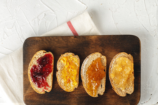 Slice of bread covered with fruit jam on wooden board close up