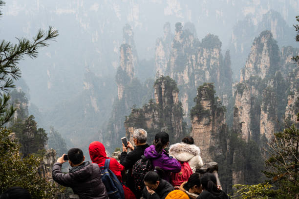 Chinese tourists taking photos of the stunning Zhangjiajie stone forest landscape from a viewpoint in Hunan province. Zhangjiajie, China - February 3 2019: Chinese tourists taking photos of the stunning Zhangjiajie stone forest landscape from a viewpoint in Hunan province. zhangjiajie stock pictures, royalty-free photos & images