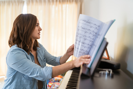 A beautiful woman present at home is busy in practicing her piano lesson .