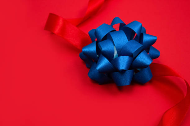 Top view on decorative blue ribbon bow on red background with copy space for text. Festive composition for greeting card design, giving presents, holidays sale or giveaway concept. Selective focus