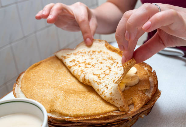 Hands wrap a pancake with banana slices. Selective focus. stock photo