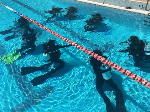 Group of unrecognizable scuba divers exercising an underwater scuba diving in a swimming pool.