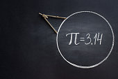 The Greek letter Pi, the ratio of the circumference of a circle to its diameter, is drawn in chalk on a black chalkboard with a compass in honor
