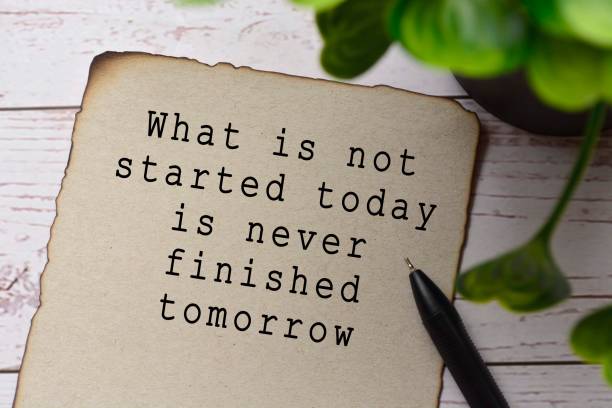 Motivational and inspirational quote on burnt edge brown paper with blurred green plant on wooden desk - What is not started today is never finished tomorrow stock photo