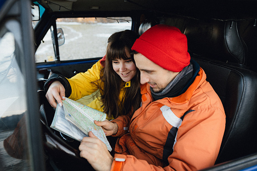 Young couple sitting in an old van, reading a map, searching for directions for their road trip route in winter