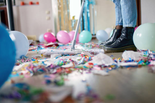 Woman with pushbroom cleaning mess of floor in room after party confetti Woman with pushbroom cleaning mess of floor in room after party confetti, morning after party celebration, housework, cleaning service after party stock pictures, royalty-free photos & images