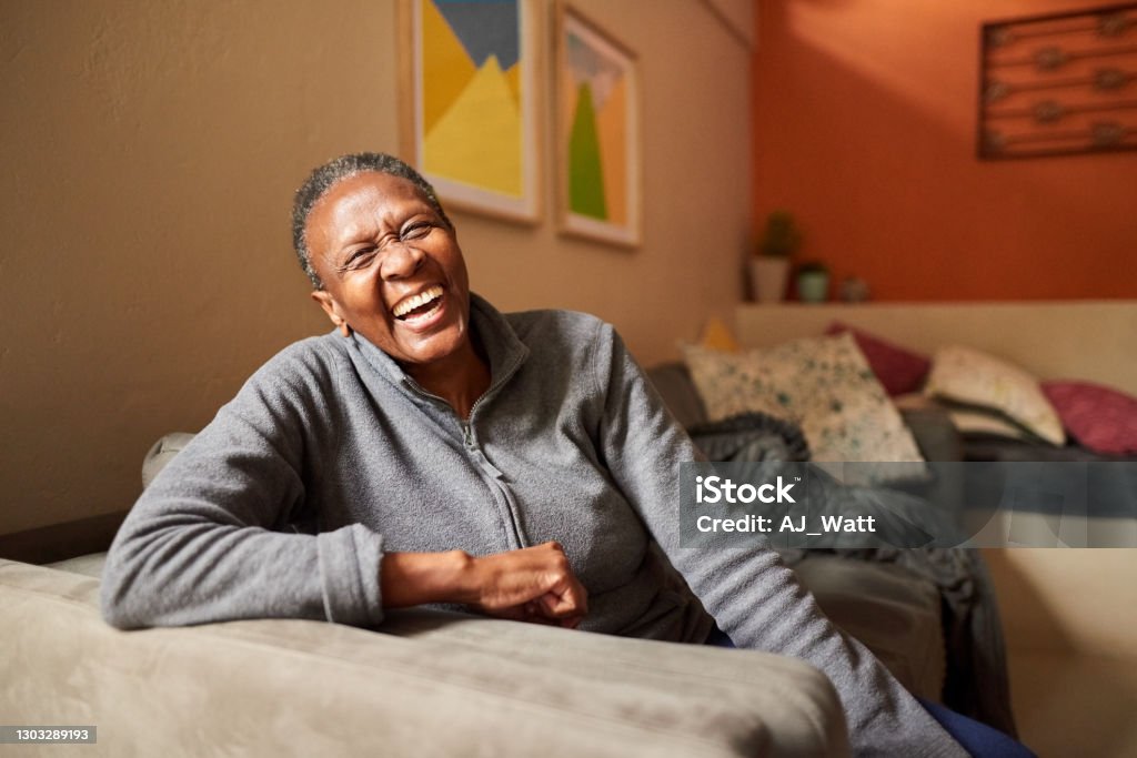 Laughing senior woman at home Portrait of a cheerful senior woman sitting on sofa in the living room and laughing Senior Adult Stock Photo
