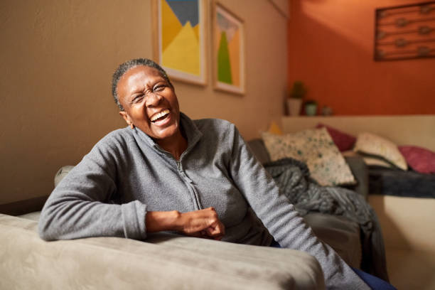 Laughing senior woman at home Portrait of a cheerful senior woman sitting on sofa in the living room and laughing 65 69 years stock pictures, royalty-free photos & images
