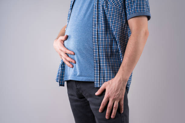 homme de graisse avec le ballonnement et la douleur abdominale, corps masculin de poids excessif sur le fond gris - abdomen photos et images de collection