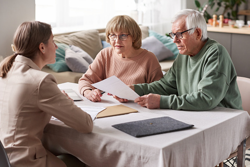 Senior couple sitting at the table with financial advisor reading documents and consulting in the room