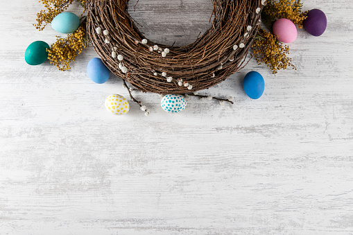 Easter wreath background with colored eggs on white wooden table