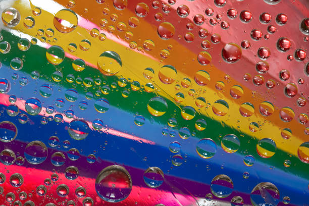 istock Rainbow. Multicolored drops of water are located against a red background with strips of rainbow colored paper. 1303301318