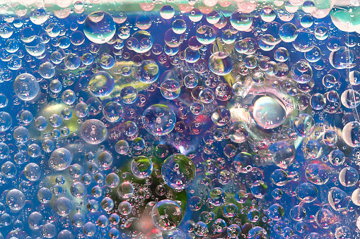 Transparent drops of water are located against a blue background with multicolored balls. Abstract fantasy. 3D render.