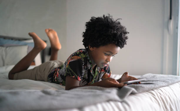 istock Boy lying in bed playing games on digital tablet at home 1303302438