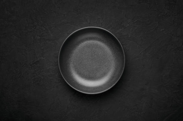 istock An empty black bowl on dark slate table top. Rough ceramic bowl background with copy space 1303303761