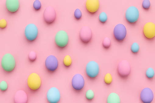 Pastel colored Easter eggs scattered on pink background. Easter Day colorful abstract flat lay.