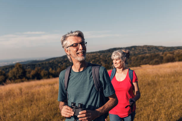 active senior couple with backpacks hiking in nature. - senior adult mountain hiking recreational pursuit imagens e fotografias de stock