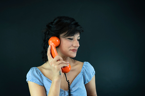Studio shot of a young woman holding a telephone while wearing 80s clothing